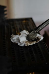 Nettoyage rapproché d'une pince utilisant un tissu sale pour nettoyer une grille de barbecue, mettant l'accent sur l'hygiène.