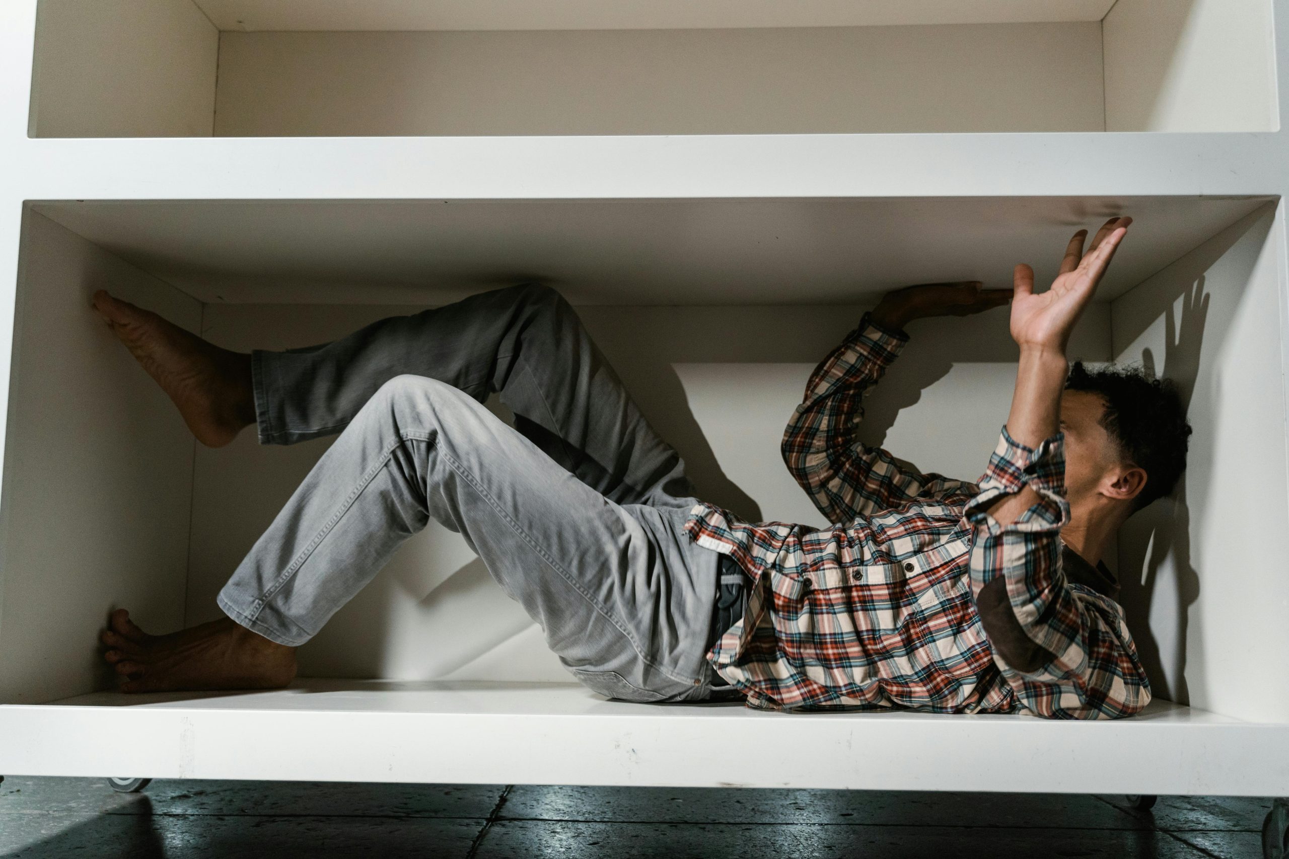 Un homme en chemise à carreaux manifeste une sensation de claustrophobie en étant à l'intérieur d'un petit meuble, évoquant des émotions d'anxiété et de peur.