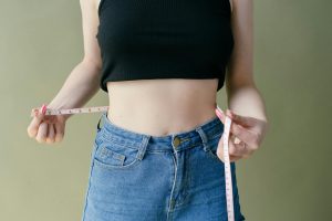 Une femme en jean et haut court utilise un mètre ruban pour vérifier son tour de taille.
