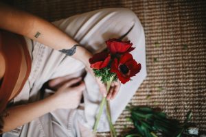 From above of crop anonymous person in casual clothes sitting with bouquet of red poppy flowers on carpet De haut, une personne anonyme en vêtements décontractés assise avec un bouquet de coquelicots rouges sur un tapis.
