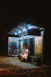 Un couple attendant à un arrêt de bus faiblement éclairé la nuit, créant une scène urbaine sereine.