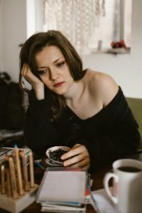 Une femme pensive assise à l'intérieur, tenant une tasse de café et réfléchissant.