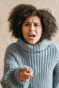 An expressive woman in a cozy sweater pointing and shouting indoors. Une femme expressive en pull douillet pointant du doigt et criant à l'intérieur.