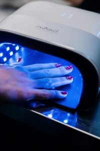 Une main avec des motifs de nail art rouges en train de durcir sous une lampe UV dans un salon de manucure professionnel.