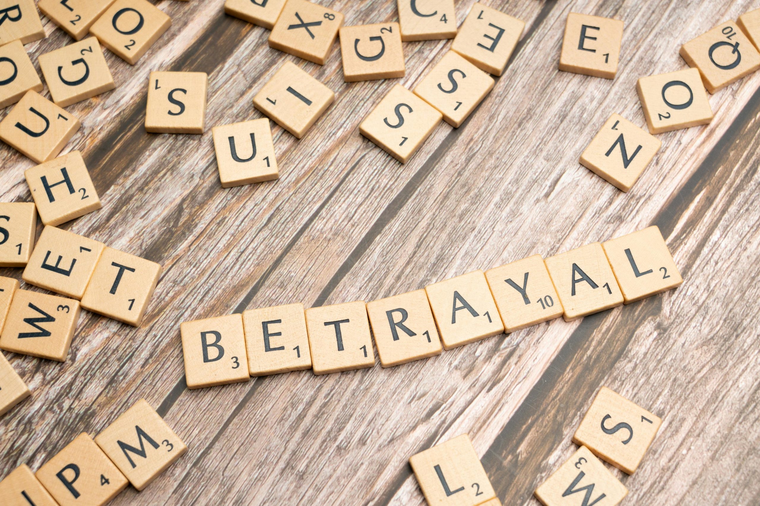Bois de lettres en bois épelant "Betrayal" sur une surface rustique en bois, évoquant des thèmes de trahison et de malhonnêteté.