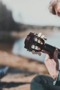 Close-up d'une personne jouant d'une guitare acoustique en plein air près d'un plan d'eau calme, créant un moment musical serein.