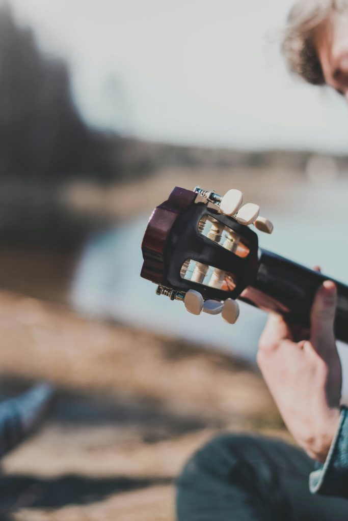 Close-up d'une personne jouant d'une guitare acoustique en plein air près d'un plan d'eau calme, créant un moment musical serein.