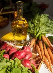 Colorful radishes and carrots with olive oil bottle in natural light. Des radis et carottes colorés avec une bouteille d'huile d'olive sous une lumière naturelle.