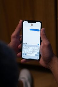 Close-up de mains envoyant un message sur un smartphone en intérieur, illustrant la communication moderne.