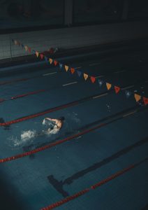 Athlète nageant le papillon dans une piscine intérieure faiblement éclairée, concentré sur l'entraînement.