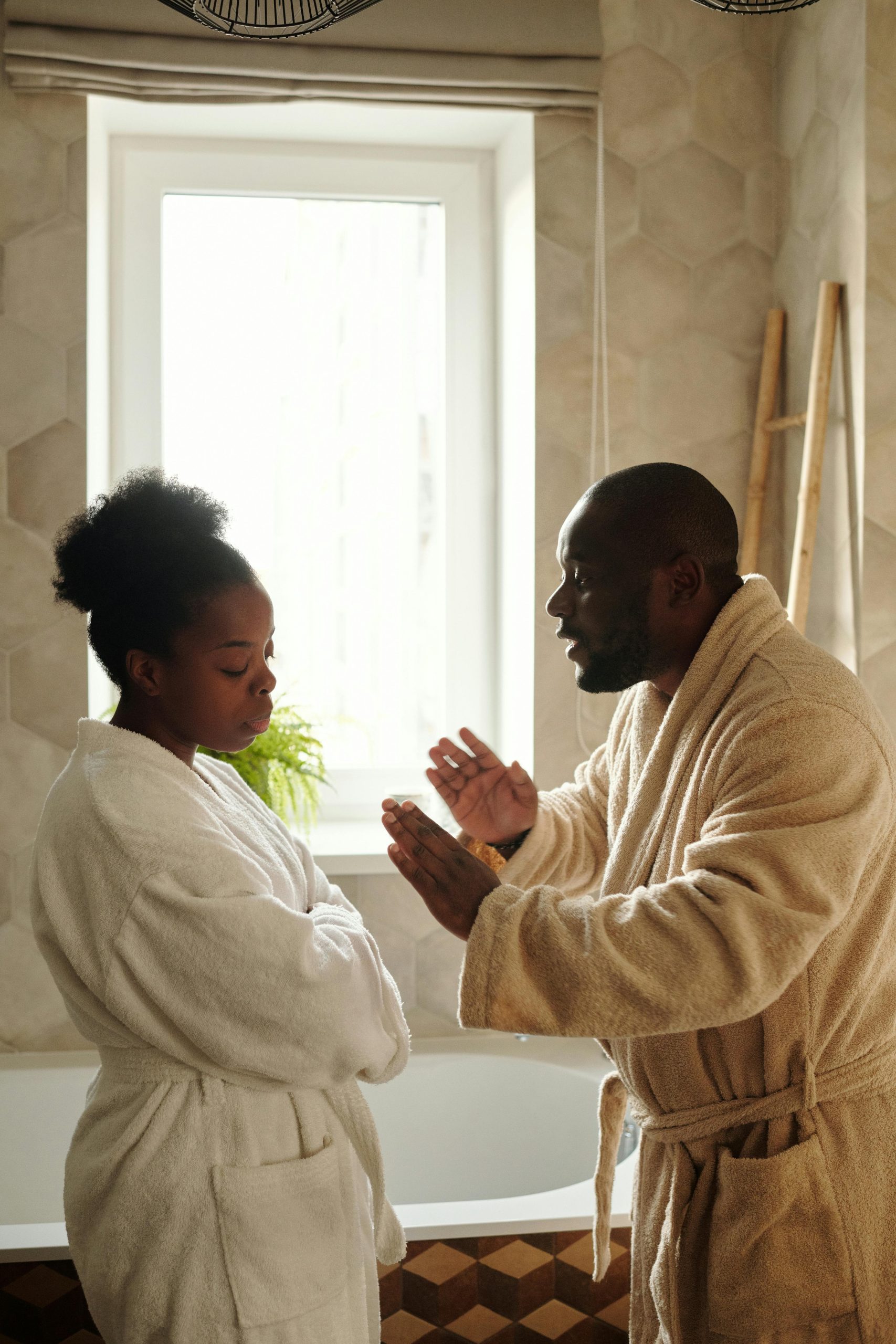 A couple emotionally discussing while wearing bathrobes in a bathroom. Un couple discutant émotionnellement vêtu de peignoirs dans une salle de bain.