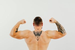 Shirtless homme exhibant ses tatouages et ses biceps en se contractant dans un studio