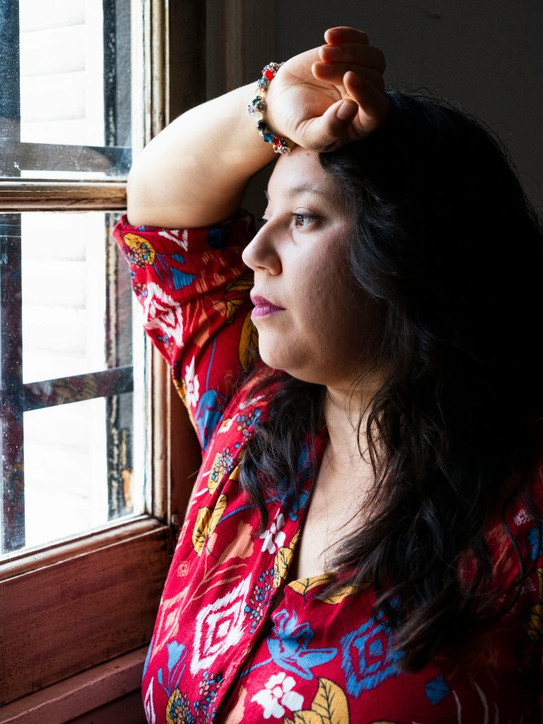 Adult woman in colorful outfit gazing out the window, lost in thought. Femme adulte en tenue colorée regardant par la fenêtre, perdue dans ses pensées.