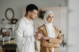 A man offering a flower to a woman in a hijab indoors, capturing a romantic moment. Un homme offrant une fleur à une femme en hijab à l'intérieur, capturant un moment romantique.