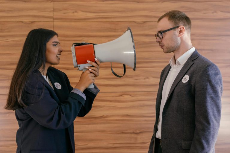 A woman using a megaphone to confront a man in a suit indoors, symbolizing political debate. Une femme utilisant un mégaphone pour confronter un homme en costume à l'intérieur, symbolisant un débat politique.