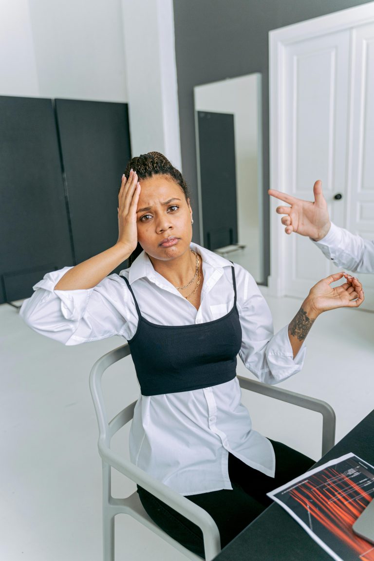 A woman shows confusion as a hand gestures towards her in an office setting. Une femme montre de la confusion alors qu'une main fait des gestes vers elle dans un cadre de bureau.