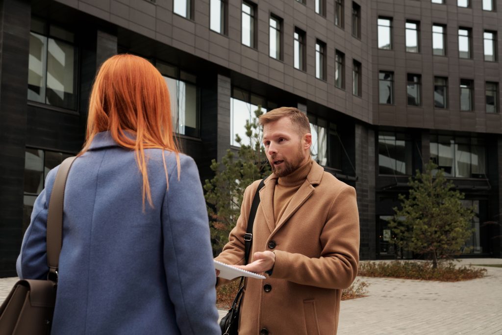 Two business professionals in conversation outside an urban office building. Deux professionnels du secteur tertiaire en conversation devant un immeuble de bureaux urbain.