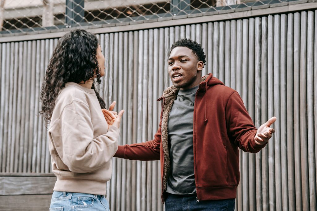 Petit ami afro-américain en colère et petite amie ethnique se regardant l'un l'autre tout en ayant une dispute émotionnelle dans la rue près d'une clôture en bois