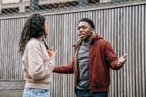 Petit ami afro-américain en colère et petite amie ethnique se regardant l'un l'autre tout en ayant une dispute émotionnelle dans la rue près d'une clôture en bois