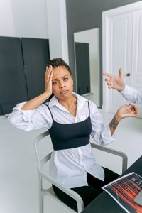 A woman shows confusion as a hand gestures towards her in an office setting. Une femme affiche de la confusion alors qu'une main gesticule vers elle dans un cadre de bureau.