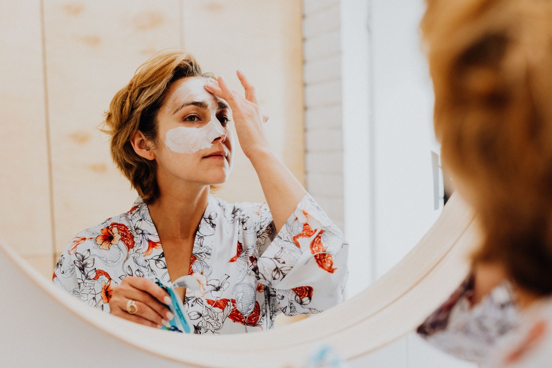 Femme applique un soin du visage devant un miroir